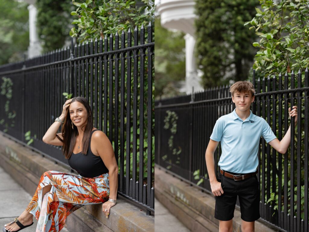 A woman in a black tank top and vibrant floral pants sits on a stone ledge next to a black fence, casually resting her hand on her head. Beside her, a young boy in a light blue polo and black shorts stands, holding onto the same fence, both smiling.