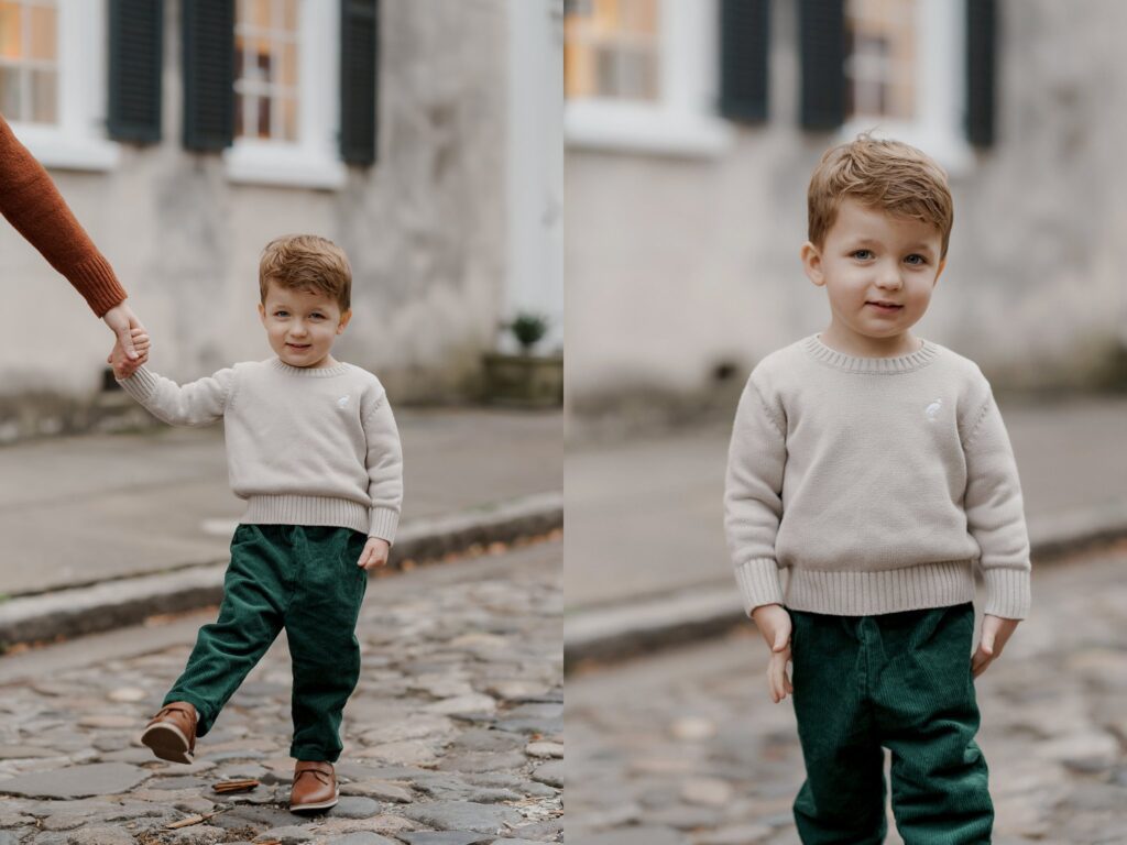 A young child with short brown hair wearing a beige sweater, green pants, and brown shoes is shown in two side-by-side images. In the left image, the child is holding an adult's hand while walking on a cobblestone street. In the right image, the child stands alone.