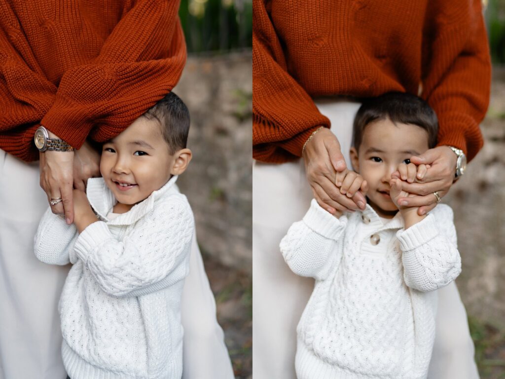 A young child in a white sweater stands in front of an adult wearing an orange sweater, smiling in one photo and playfully covering his mouth with the adult’s hands in the other, perfectly captured by a photographer Charleston SC.