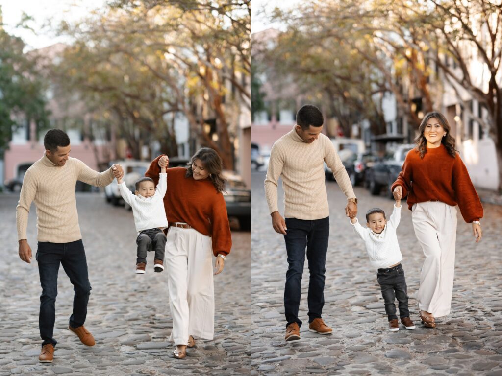  cheerful family walks along the cobblestone streets in downtown Charleston, SC, lifting their young son into the air as he laughs with joy. The parents, dressed in coordinating fall outfits, smile at him lovingly. Captured by photographer Charleston SC during a candid family photo session in the historic district.