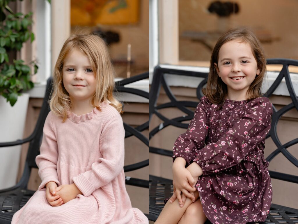 Two young girls sit side by side on a decorative outdoor bench, smiling sweetly with hands in their laps. Their pastel dresses and joyful expressions capture the heartwarming moments often seen during mini sessions Charleston SC.