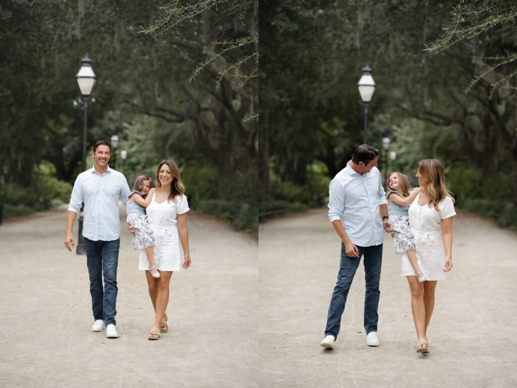 A smiling man and woman walk down a tree-lined path, holding hands with a young girl in a floral dress. Captured by a family photographer in Charleston SC, the trio appears happy and relaxed as they playfully swing the child between them.