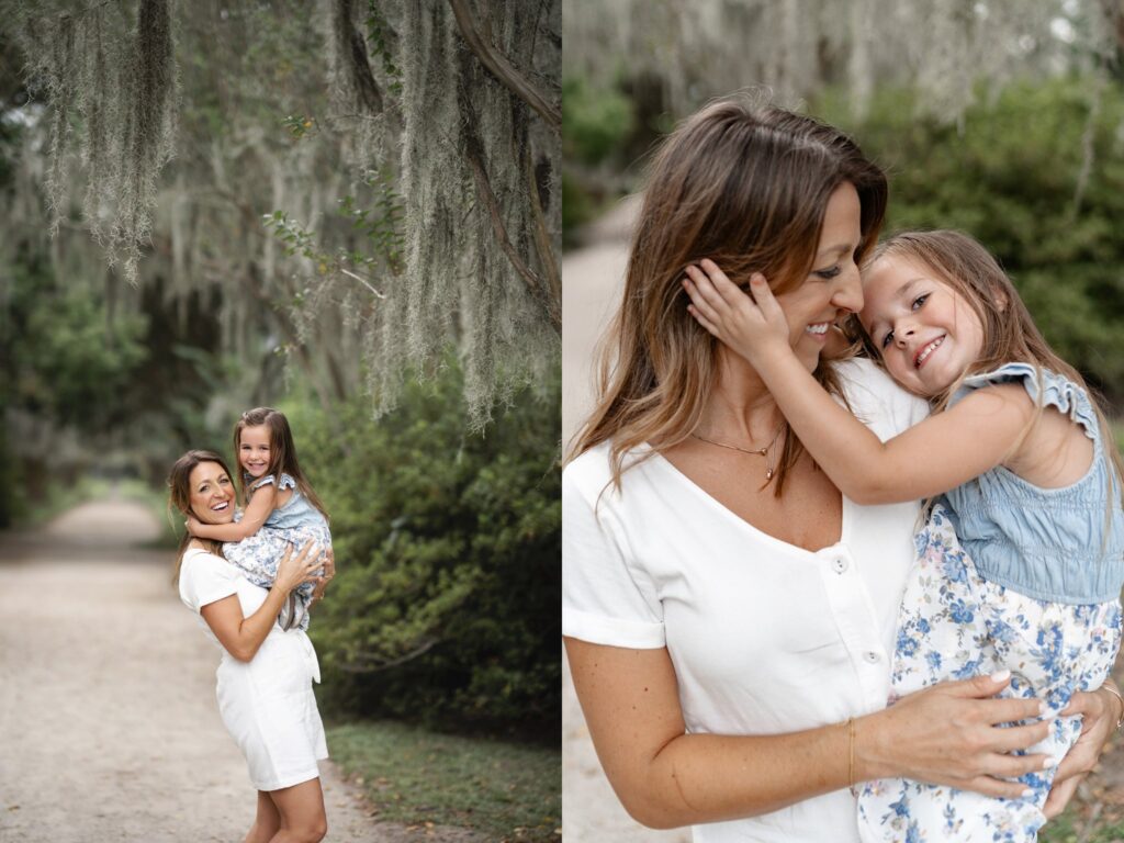 A woman in a white outfit holds a smiling young girl in a blue dress. Captured by a family photographer in Charleston SC, they embrace happily on a tree-lined path with hanging moss, sharing a joyful and affectionate moment outdoors.